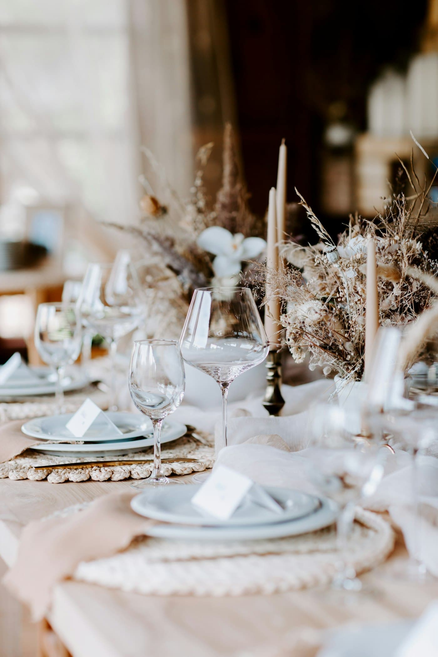 Mesa posta para casamento com pratos claros, taças, sousplats de palha e velas finas