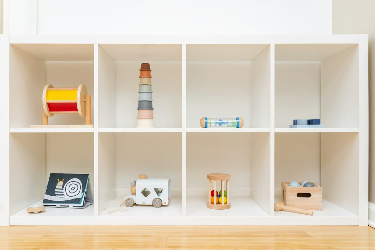 Estante branca de nichos com brinquedos de madeira, livros e cestinhos para o primeiro ano