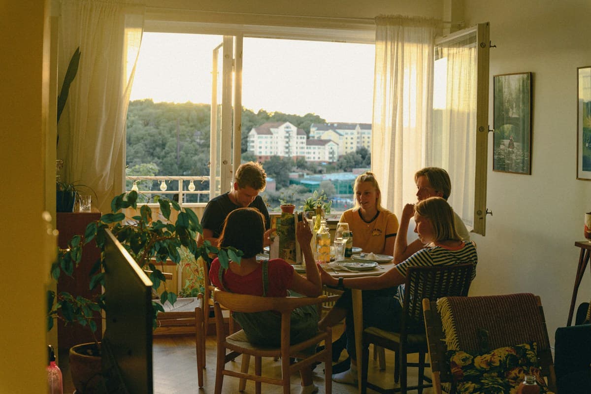 Amigos jantando em volta da mesa de um apartamento iluminado pela luz do fim de tarde