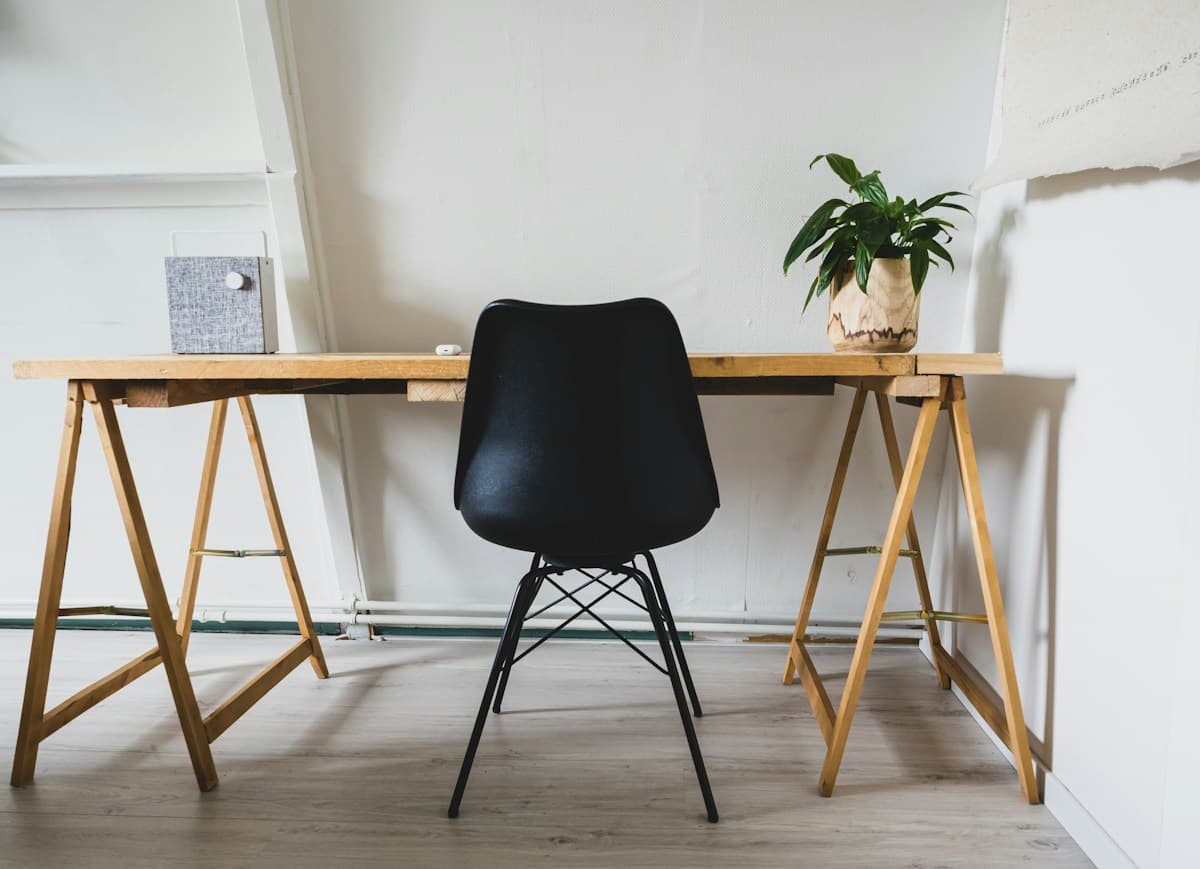 Home office minimalista com mesa de cavaletes de madeira, cadeira preta e vaso de planta