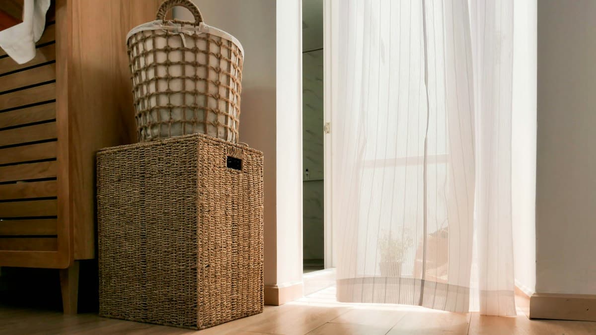 Cestos de fibra natural empilhados ao lado de cortinas brancas e móvel de madeira
